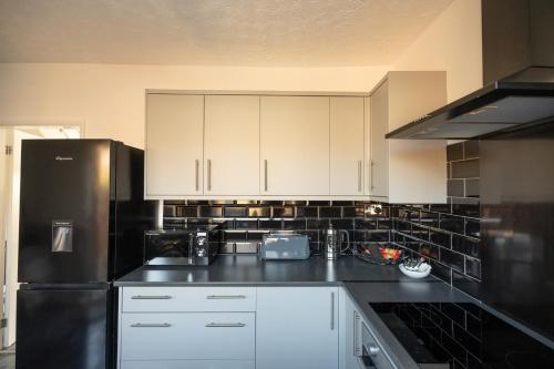 uma cozinha com armários brancos e um frigorífico preto em Brinkburn House By Horizon Stays em Stockton-on-Tees