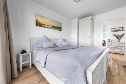 a white bedroom with a large bed with blue pillows at Am Yachthafen in Olpenitz