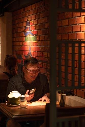 a man sitting at a table looking at his cell phone at Solaria Hanoi Hotel in Hanoi