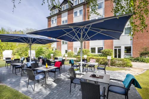 een patio met tafels, stoelen en parasols bij Best Western Hotel Prisma in Neumünster