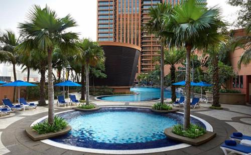 uma piscina com palmeiras, cadeiras e guarda-sóis azuis em KLCC, Kuala Lumpur, Bukit Bintang at Times Square Hotel em Kuala Lumpur
