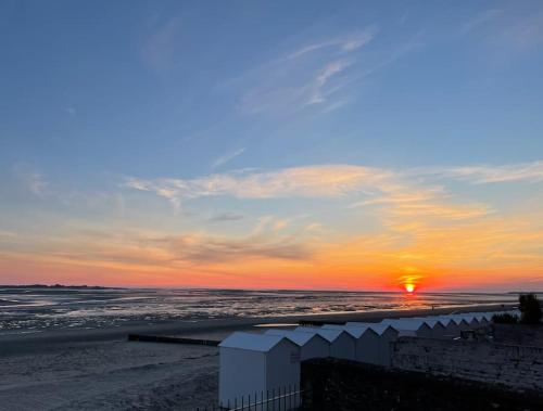 una puesta de sol sobre una playa con el océano en En plein coeur du Crotoy, un pied à terre en Baie, en Le Crotoy
