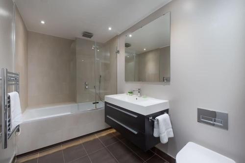 a bathroom with a sink and a tub and a sink and a mirror at West Kensington by Capital in London