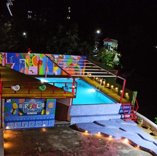 a swimming pool at night with a brightly colored wall at Gods County Hotels & Resorts in Tarapith