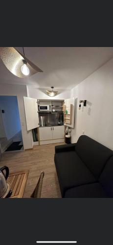 un salon avec un canapé noir et une cuisine dans l'établissement Chambre 7 kitchenette Les gites de la Gare, à Mussidan