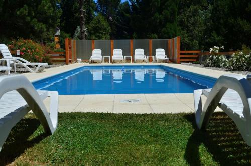 a swimming pool with white chairs and a group at Cabañas Villa Labrador con costa de lago in San Carlos de Bariloche