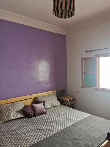 - une chambre avec un lit et un mur violet dans l'établissement Chez Marie, à Al Ghar