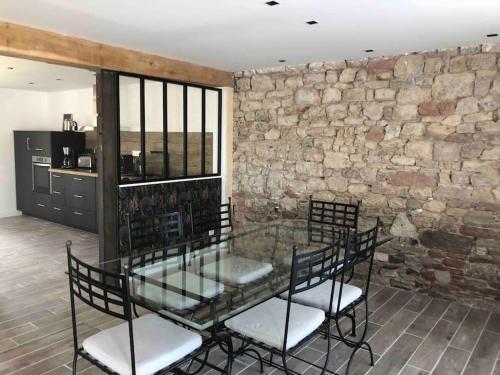 - une table et des chaises en verre dans une pièce dotée d'un mur en pierre dans l'établissement Maison entièrement renovee, à Meyssac