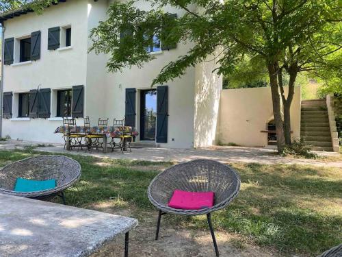 Deux tables avec des chaises colorées devant un bâtiment dans l'établissement Maison les Acacias, à Millau