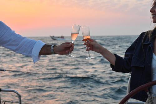 two people holding up wine glasses in the ocean at Noite a bordo de um veleiro em Viana do Castelo in Viana do Castelo