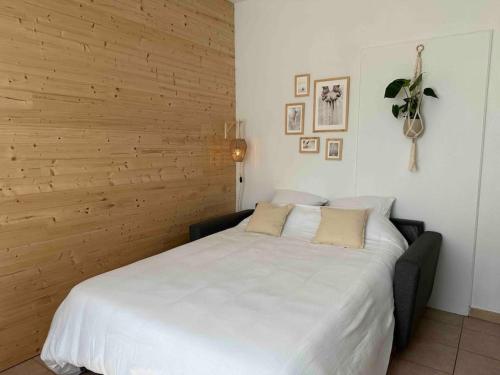 a white bed in a room with a wooden wall at Appartement lumineux Parking Privé Gratuit in Bourg-en-Bresse