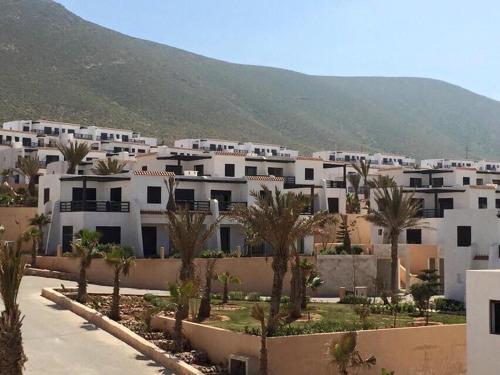 um grupo de edifícios brancos com palmeiras e uma montanha em Aglou center em Zaouia Sidi Ouaggag