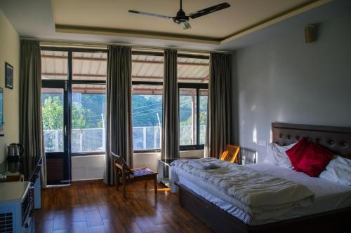 a bedroom with a bed and large windows at Dhauladhar View Village Resort in Dharmsāla