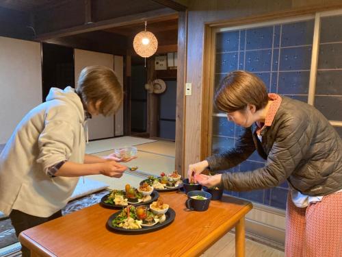 two women standing in a kitchen with plates of food at ラコマハウス in Takinohai