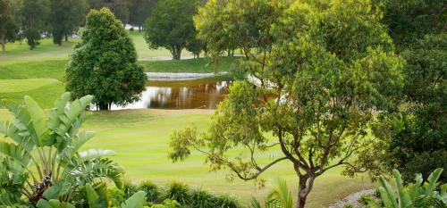 a golf course with a pond and trees in the foreground at Byron Links Apartments in Byron Bay