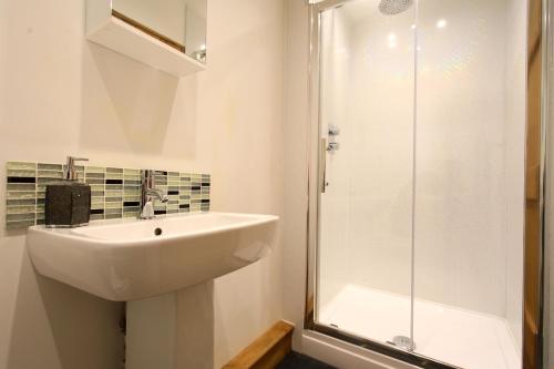 a white bathroom with a sink and a shower at Woodshed Cottage in Ashbourne