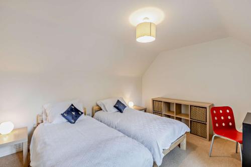 1 dormitorio con 2 camas y silla roja en Tall Trees. Luxury North Cotswold cottage, en Banbury