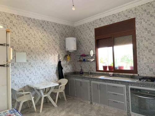 eine Küche mit einem Waschbecken, einem Tisch und einem Fenster in der Unterkunft villa avec piscine à louer in Bir Jedíd Saint-Hubert