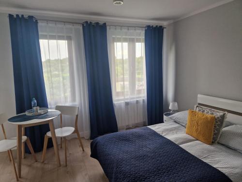 sypialnia z niebieskimi zasłonami, łóżkiem i stołem w obiekcie Pokoje Gościnne Cztery Wiatry we Fromborku