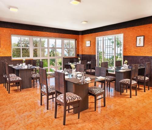 a dining room with tables and chairs and windows at Mango Hill Kodai in Kodaikānāl