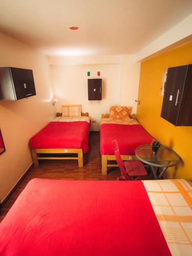 a room with two beds with red sheets and a table at The Chusay Rooftop in Cusco