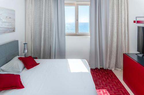 Cette chambre comprend un lit blanc avec des oreillers rouges et une télévision. dans l'établissement Lustica Bay Marina Village 3-bedroom corner apartment with a terrace and panoramic sea view, à Radovići
