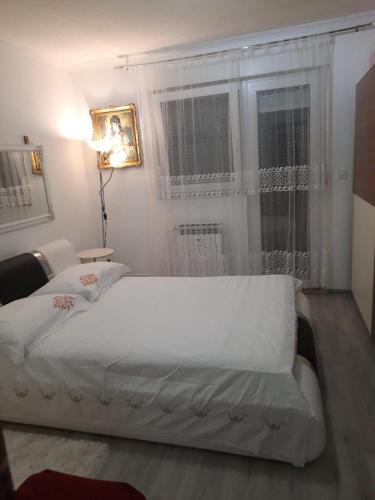 a bedroom with a white bed and a window at Nada apartman in Vukovar