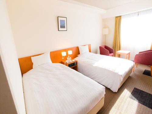 una habitación de hotel con 2 camas y una silla en Hotel Lexton Kagoshima, en Kagoshima