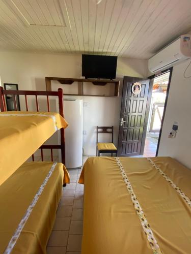 two beds in a room with a refrigerator and a tv at Pousada Aventura in Passo de Torres