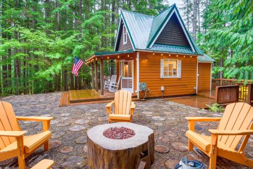 a cabin in the woods with two chairs and a table at Adorable A-Frame Cabin, Steps to Lake Cushman! in Hoodsport