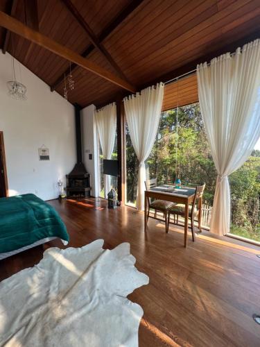 a bedroom with a bed and a table and windows at Zatara's Lodge - Monte Verde MG in Camanducaia