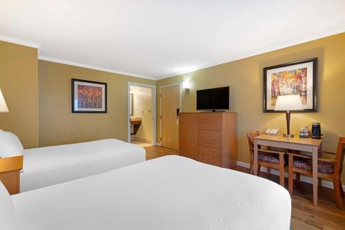 a hotel room with two beds and a desk and a television at Best Western Plus Windjammer Inn & Conference Center in Burlington