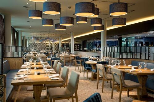 un restaurant avec des tables en bois, des chaises et des lumières dans l'établissement Hilton Amsterdam Airport Schiphol, à Schiphol