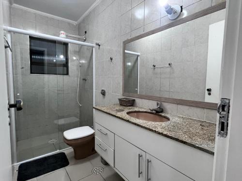 uma casa de banho com um lavatório, um chuveiro e um WC. em AeK apartamento conforto praia em Peruíbe