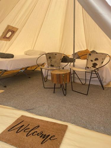 a tent with a bed and two chairs and a welcome mat at Box Flat Belle Off Grid Glamping in Lightning Ridge