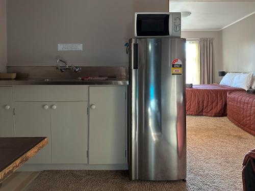 a kitchen with a refrigerator with a microwave on top of it at The Crossing Lodge & Backpackers in Erua