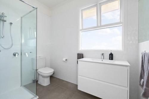 a white bathroom with a toilet and a glass shower at Botanical Oasis in Frankston