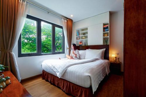 a woman sitting on a bed in a bedroom with a window at The Bloom Classic - Hotel and Bistro in Hanoi