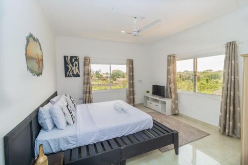 Schlafzimmer mit einem Bett, einem TV und Fenstern in der Unterkunft Chameleon house diani in Ukunda