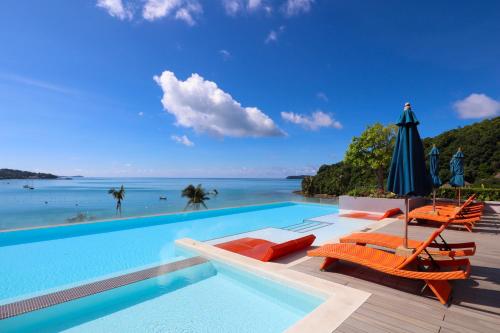 a swimming pool with chairs and an umbrella and the ocean at Bandara Beach Resort, Phuket in Panwa Beach