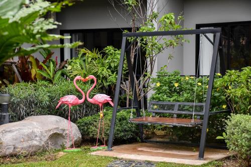 two flamingos standing next to a swing and a bench at JINGLE JUNGLE RESORT KHAOYAI in Mu Si