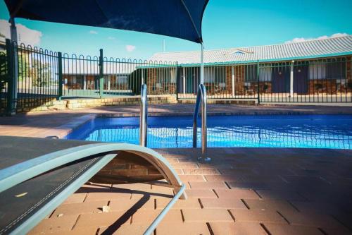 a swimming pool with an umbrella next to it at Almond Inn Motel in Tamworth