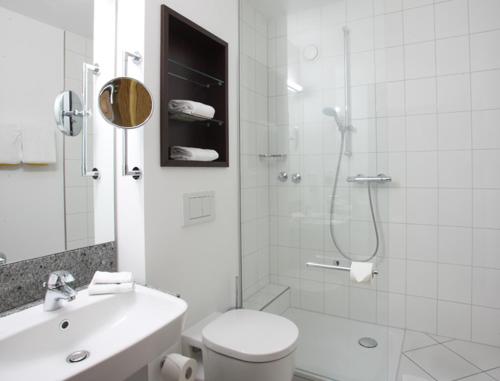 a white bathroom with a shower and a toilet and a sink at Parkhotel Frankfurt-Rödermark in Rödermark
