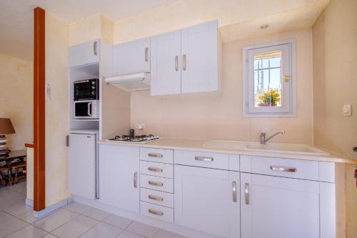 une cuisine avec des armoires blanches, un évier et une fenêtre dans l'établissement Appartement 4 personnes Le Tignet, à Le Tignet