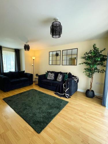 a living room with black couches and a green rug at Majestic House - Milton Keynes Serviced Accommodation in Milton Keynes