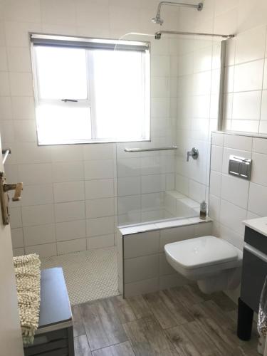 a white bathroom with a toilet and a window at Fairhaven Beachhouse & Pool Blouberg seaside in Bloubergstrand
