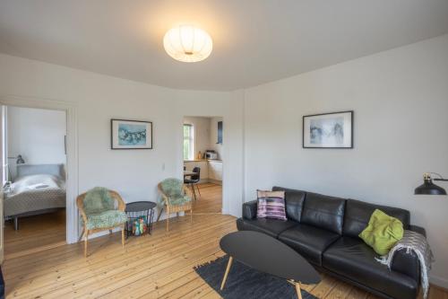 una sala de estar con un sofá de cuero negro y sillas en Central Lyngby Apartments, en Kongens Lyngby