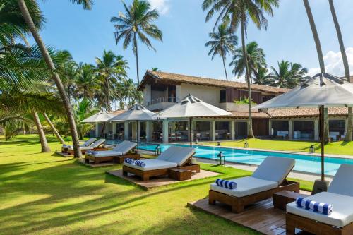 un complexe avec une piscine, des chaises et des palmiers dans l'établissement Villa Thamburu, Bentota, à Bentota