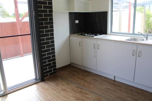 una cocina con armarios blancos, fregadero y ventanas en Stay at Linton, en Loganlea