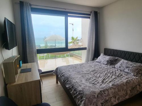 a bedroom with a bed and a view of the ocean at Appartement Plage des Nations Prestigia Front Mer avec grand Jardin in Sidi Bouqnadel